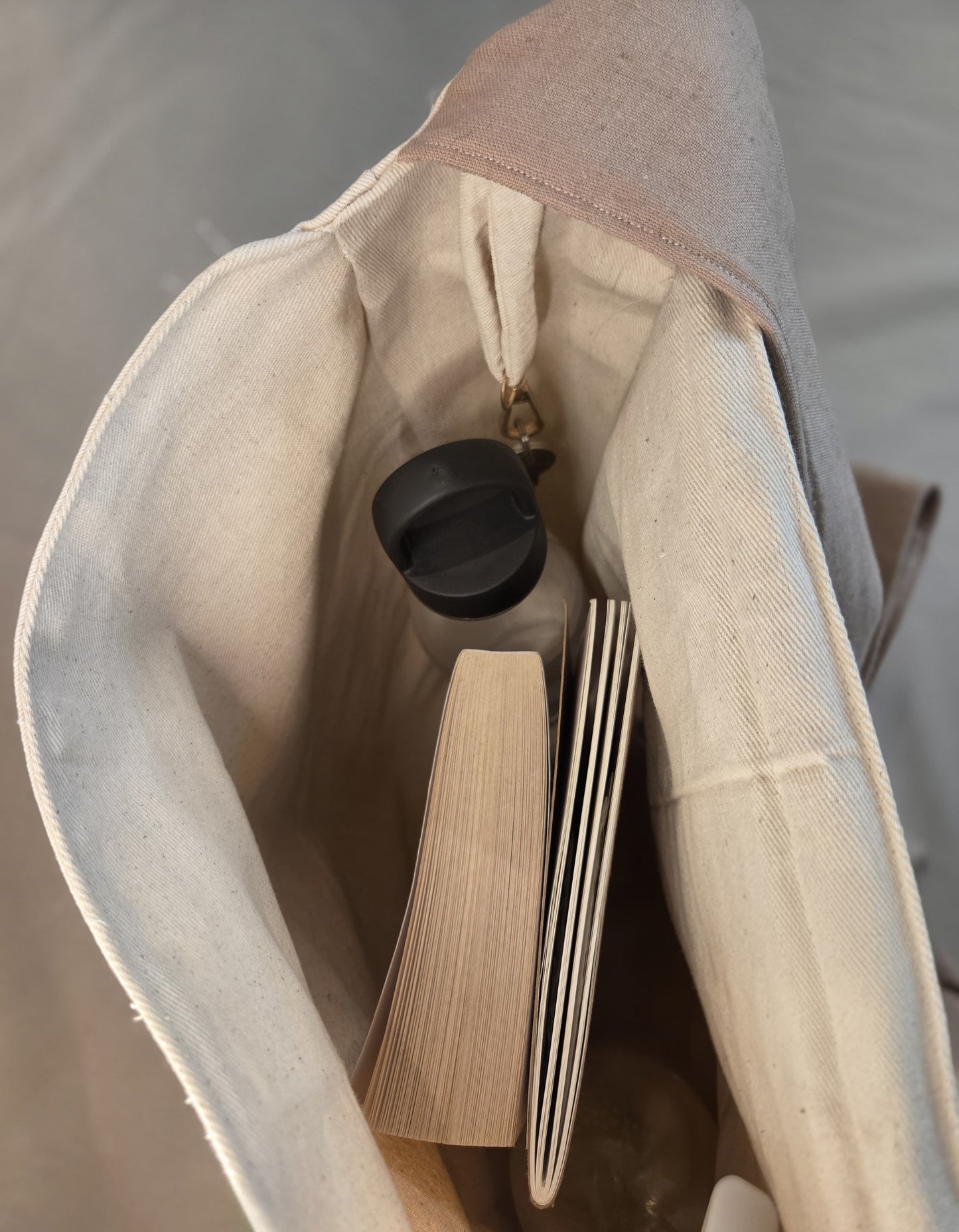 Close-up of a beige bag with a black bottle and a book inside.
